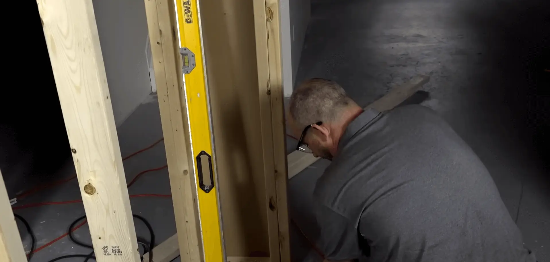 A contractor working on framing a basement wall, using a level to ensure accuracy. Get expert help finishing your basement today!