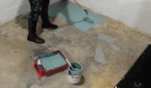 A person painting a concrete basement floor with epoxy paint to create a smooth, finished surface—start your basement floor transformation today.