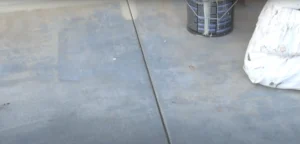 A close-up view of a concrete basement floor with a paint can and supplies, prepared for painting to improve durability and aesthetics.